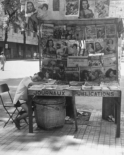 Một trẻ bán báo đang nghĩ mệt bên cạnh sạp báo và tạp chí. 
