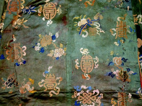 Hoa văn vạn thọ trên áo dài bằng vải đoạn mầu quan lục của vua Bảo Đại.